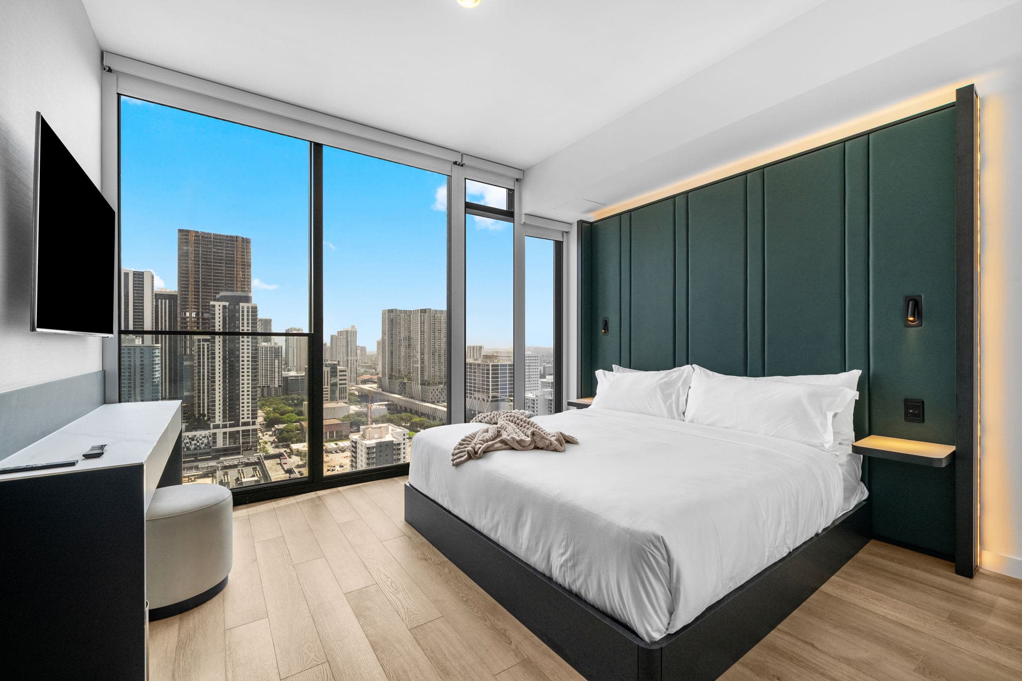 Bed beside floor-to-ceiling city-view windows.